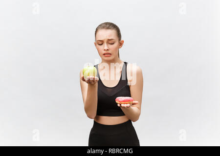 Junge Frau die Wahl zwischen Donut und Apple auf weißem Hintergrund. Ernährung Lebensmittel Konzept Stockfoto