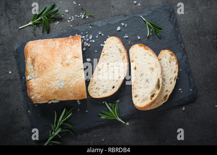 Italienische ciabatta Brot auf schwarzem Schiefer mit Kräutern und Oliven, Ansicht von oben. Stockfoto