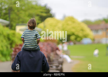 Happy Family Konzept - verschwommenes Bild des Kindes, die auf Vater Hals sitzt und Spaß im Park an einem sonnigen Tag Stockfoto