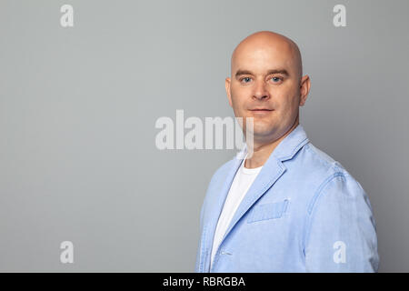 Glatzköpfige Mann in einer blauen Jacke gegen eine graue Wand Stockfoto
