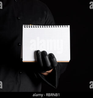 Koch in schwarzer Uniform und schwarzem Latex Handschuhe mit einem leeren, schwarzen Hintergrund, Notebook Stockfoto