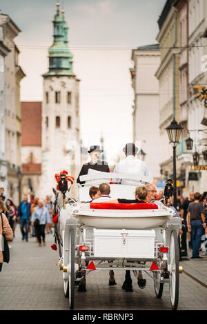 Krakau, Polen - 28. August 2018: Altmodische Coach Schlitten bewegen sich auf Straßen der Altstadt im Sommer Tag. Besichtigung von historischen Stätten. Blick auf die Kirche von S Stockfoto