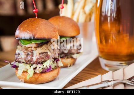 Zwei Schieberegler angehäufte Höhe mit Toppings, serviert mit Bier und Pommes Frites Stockfoto