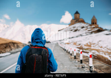 Stepantsminda, Gergeti, Georgia. Man Touristen Backpacker Reisender Fotograf zu Fuß zur Kirche der Heiligen Dreifaltigkeit - Tsminda Sameba. Schönen georgianischen Land Stockfoto