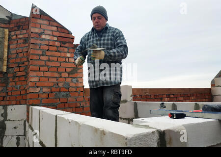 Mit Hilfe eines glutenhaltigen Lösung, der Arbeiter eine Mauer errichtet von Gas Bausteine 2018 Stockfoto