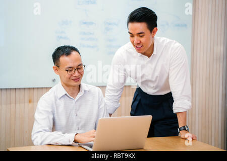 Porträt von zwei asiatischen Geschäftsleuten, die eine geschäftliche Besprechung in einem Tagungsraum mit einer Tafel im Hintergrund. Sie sind beide auf der Suche nach einem Notebook. Stockfoto