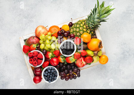 Rainbow Früchte in Holz- fach, Pflaumen Erdbeeren Himbeeren Orangen, Äpfel, Kiwis, Weintrauben, Heidelbeeren mango Kaki Ananas auf Weiß Stockfoto