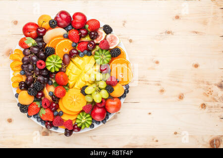 Gesunde Obstteller, Pflaumen Erdbeeren Himbeeren Orangen, Äpfel, Kiwis, Weintrauben, Heidelbeeren mango Kaki auf Holztisch, Ansicht von oben Stockfoto