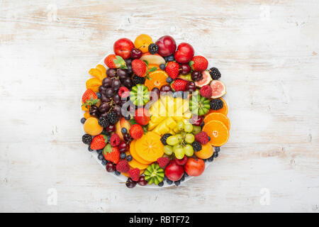 Gesunde Obstteller, Pflaumen Erdbeeren Himbeeren Orangen, Äpfel, Kiwis, Weintrauben, Heidelbeeren mango Kaki auf die weiße Holztisch Stockfoto