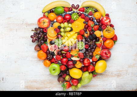 Herz aus gesunden rainbow Obst Schüssel Pflaumen Erdbeeren Himbeeren, Orangen, Äpfel, Kiwis, Weintrauben, Heidelbeeren mango Kaki Ananas Stockfoto