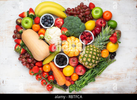 Herz aus gesunden rainbow Früchte Gemüse Beeren, Erdbeeren, Orangen, Pflaumen Trauben Brokkoli cauiliflower Mango kaki Ananas auf Holz Stockfoto