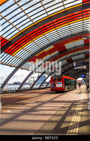 AMSTERDAM, Niederlande - 1 September, 2018: Hauptbahnhof in Amsterdam bus Plattform mit bunten Überhang gesehen mit Schiffen und Gebäuden sichtbar Stockfoto