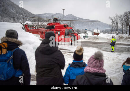 12 Januar 2019, Bayern, Schönau am Königssee: ein Hubschrauber der Stände des Typs "Super Puma" auf einem Parkplatz und wird von den Zuschauern während der Anlaufphase beobachtet. Der Helikopter ist für Wirbel der Schnee von den Bäumen auf Straßen soll und damit das Risiko einer Niederlassung Bruch zu reduzieren. Die starken Schneefälle der vergangenen Tage weiterhin den Einsatzkräften in Atem im südlichen Bayern und Neuschnee zu halten ist schon näher. Nach Angaben der Behörden mehr als 1000 Helfer sind in den südlichen Bezirken von Oberbayern eingesetzt. Foto: Lino Mirgeler/dpa Stockfoto