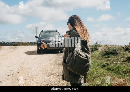 Mädchen Tourist mit einem Rucksack Reisen per Anhalter. Sie hob ihre Finger auf und versucht, das Auto ihre Reise fortsetzen zu stoppen. Stockfoto