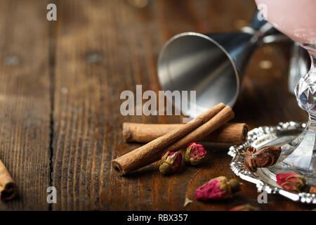 Zimt auf der Theke, auf einem hölzernen Hintergrund. Daneben Rosenblütenblätter getrocknet sind. Stockfoto