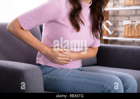 Junge Frau sitzt auf einem Sofa Leiden von Magenschmerzen Stockfoto