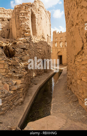 Wasserzwangsführung (aflaj) in den Gassen zwischen den halb verlassenen Schlamm Häuser von Birkat Al Mouz Stockfoto