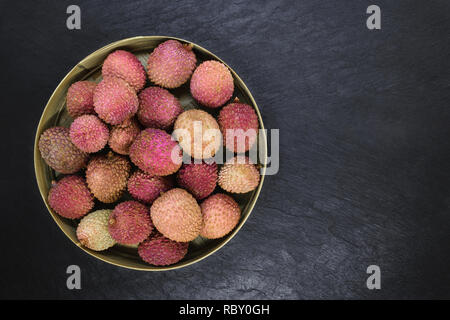 Lychees Früchte in runden Bambus Schale auf schwarzen Stein Hintergrund Oberfläche mit Kopie Raum Stockfoto