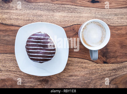 Schokolade überzogen jelly Donut und Tasse Kaffee auf hölzernen Tisch Stockfoto