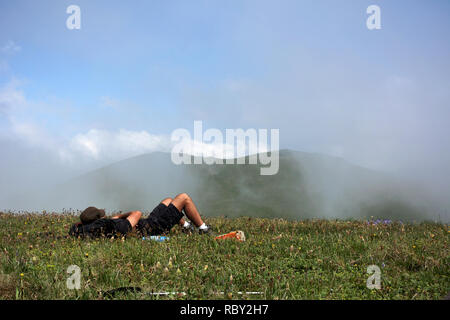 Sportlicher Mann auf dem Berg trek, Mann liegt und Ruhe. Gesunde junge Mann ruht auf Stein in Kletterte Berggipfel genießen Panoramablick während der Wanderung. Stockfoto