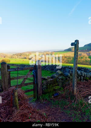 Holz- Wegweiser durch ein Tor und über einer Wiese in der Derbyshire Peak District. Stockfoto
