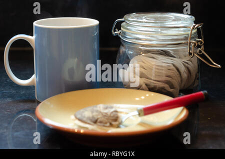 Eine blaue Tasse, ein Glas Tee Beutel eine Untertasse, Tl und gebrauchte Teebeutel auf einer Küchenarbeitsplatte. Stockfoto