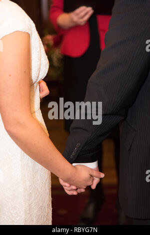 Rückansicht der Braut im weißen Kleid und der Bräutigam in der Klage halten jedes andere Hände Stockfoto
