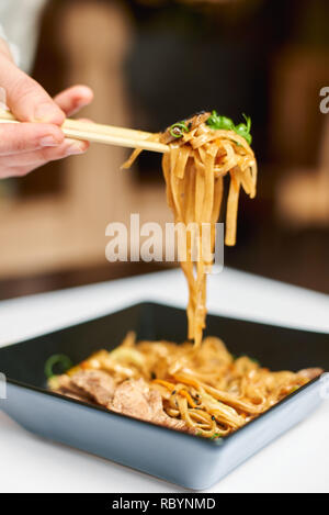 In der Nähe von Japanischen exotische Gericht in orientalischen Luxus Restaurant. Kunden genießen leckere Nudeln mit Fleisch in quadratische schwarze und weiße Platte. Gast Essen Stockfoto