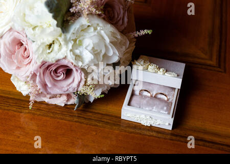 Ein paar Trauringe in einem weißen Schmuck Kästchen neben einem Hochzeit Blumenstrauß Stockfoto
