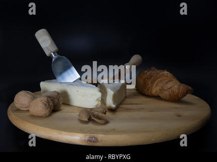 Holz- drehbare Platte mit französischem Käse genannt Brie mit einem Messer und einem französischen Croissant und Walnüsse und Mandeln Stockfoto