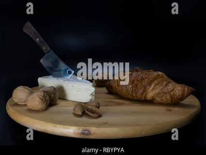 Holz- drehbare Platte mit französischem Käse genannt Brie mit einem Messer und einem französischen Croissant und Walnüsse und Mandeln Stockfoto