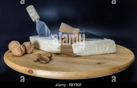 Holz- drehbare Platte mit französischem Käse genannt Brie mit einem Messer und einem französischen Croissant und Walnüsse und Mandeln Stockfoto