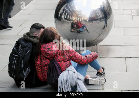 Junges Paar Touristen eine selfie mit einem Mobiltelefon sitzt auf dem Bürgersteig in eine silberne Kugel suchen im Winter London UK KATHY DEWITT Stockfoto