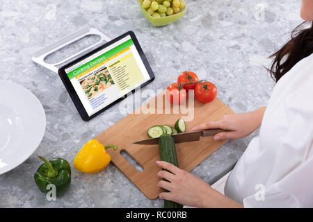 Frau Schneiden Gurken mit Messer in der Nähe Rezepte Kochen auf digitalen Tablet Bildschirm Stockfoto