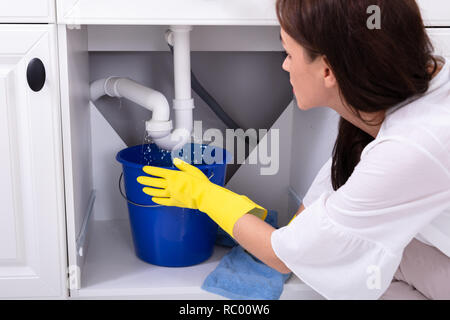 Nahaufnahme einer jungen Frau die blauen Eimer unter Wasser leckt von der Spüle Leitung Stockfoto