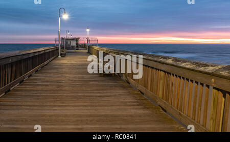 Sonnenaufgang von der Sandbridge Fishing Pier auf der kleinen Insel Park in Virginia Beach. Das Holz der Pier leuchtet durch frühen Morgen Sonne in der Clou Stockfoto