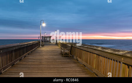 Sonnenaufgang von der Sandbridge Fishing Pier auf der kleinen Insel Park in Virginia Beach. Das Holz der Pier leuchtet durch frühen Morgen Sonne in der Clou Stockfoto