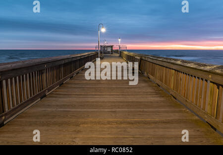 Sonnenaufgang von der Sandbridge Fishing Pier auf der kleinen Insel Park in Virginia Beach. Das Holz der Pier leuchtet durch frühen Morgen Sonne in der Clou Stockfoto