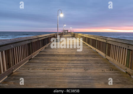 Sonnenaufgang von der Sandbridge Fishing Pier auf der kleinen Insel Park in Virginia Beach. Das Holz der Pier leuchtet durch frühen Morgen Sonne in der Clou Stockfoto