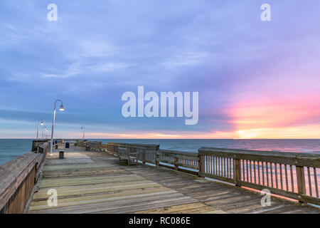 Sonnenaufgang von der Sandbridge Fishing Pier auf der kleinen Insel Park in Virginia Beach. Das Holz der Pier leuchtet durch frühen Morgen Sonne in der Clou Stockfoto