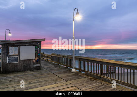 Sonnenaufgang von der Sandbridge Fishing Pier auf der kleinen Insel Park in Virginia Beach. Das Holz der Pier leuchtet durch frühen Morgen Sonne in der Clou Stockfoto