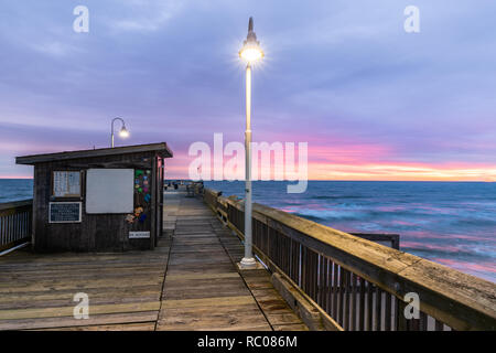 Sonnenaufgang von der Sandbridge Fishing Pier auf der kleinen Insel Park in Virginia Beach. Das Holz der Pier leuchtet durch frühen Morgen Sonne in der Clou Stockfoto