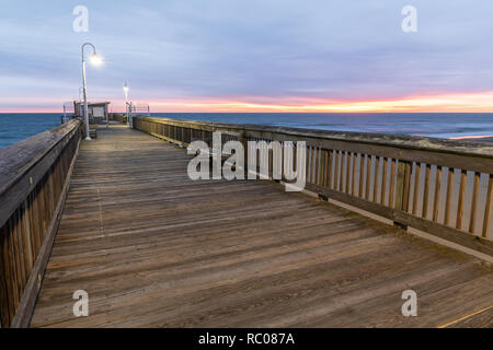 Sonnenaufgang von der Sandbridge Fishing Pier auf der kleinen Insel Park in Virginia Beach. Das Holz der Pier leuchtet durch frühen Morgen Sonne in der Clou Stockfoto