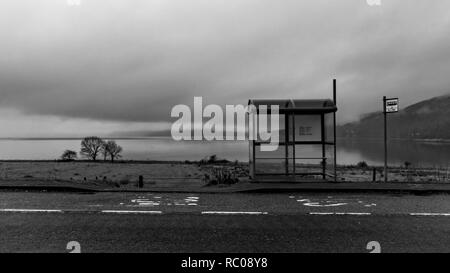 Schwarz-weiß Bild von der Bushaltestelle in Country Side area up North in Schottland in der Nähe von Fort William. Leere Straße und See auf dem Hintergrund Stockfoto