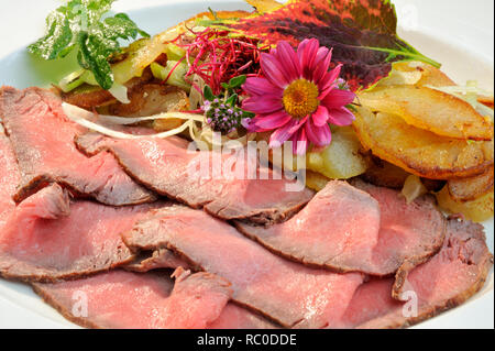 Roastbeef mit Bratkartoffeln, dekoriert mit essbaren Sky und Kräutern | Roastbeef mit Braten oder Bratkartoffeln Stockfoto