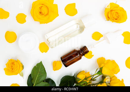 Aromatische botanische Kosmetik. Hautpflege Home Spa Behandlung mit gelben Blütenblättern, Rosenblüten, eine Flasche Öl, Rosenwasser. Stockfoto