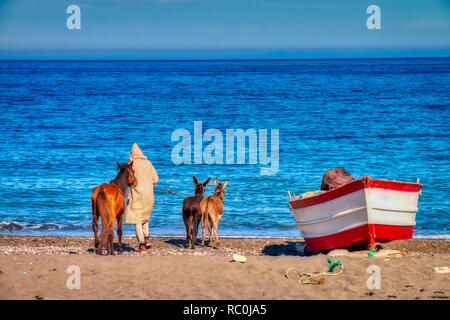 Oued Laou, Chefchaouen, Marokko - November 3, 2018: Ein junger Mann im traditionellen marokkanischen Kleidung geht seinen Esel am Strand von Oued Laou, einem kleinen zu Stockfoto