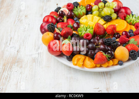 Gesunde Obstteller, Pflaumen Erdbeeren Himbeeren Orangen, Äpfel, Kiwis, Weintrauben, Heidelbeeren mango Kaki auf Holztisch, kopieren Platz für Text Stockfoto