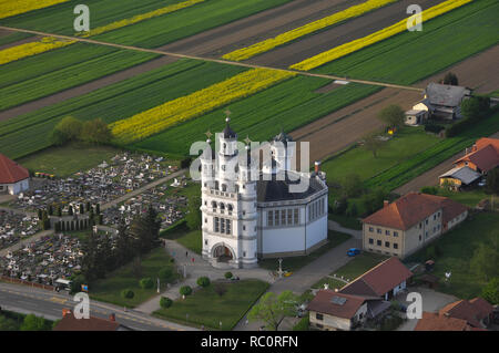 Luftaufnahme der Kirche der Heiligen Dreifaltigkeit in einem kleinen Dorf in den Sonnenuntergang, ein Friedhof neben der Kirche, einzigartige Architektur, Odranci, Slowenien Stockfoto