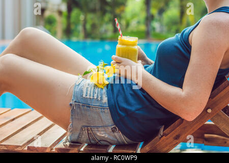 Junge Frau hält ein Smoothie mango auf dem Hintergrund der Pool. Fruit Smoothie - gesunde ernährung Konzept. Nahaufnahme von detox Smoothie mit Mann Stockfoto